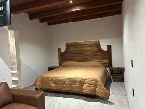Cozy retreat with a comfortable bed, nightstand, and leather chair, set against a stone wall and sloped ceiling.