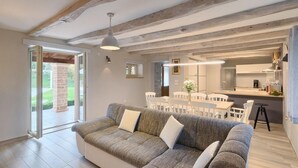 Een moderne woonkamer met een bank, eettafel en stoelen. In de achtergrond is een keuken te zien.