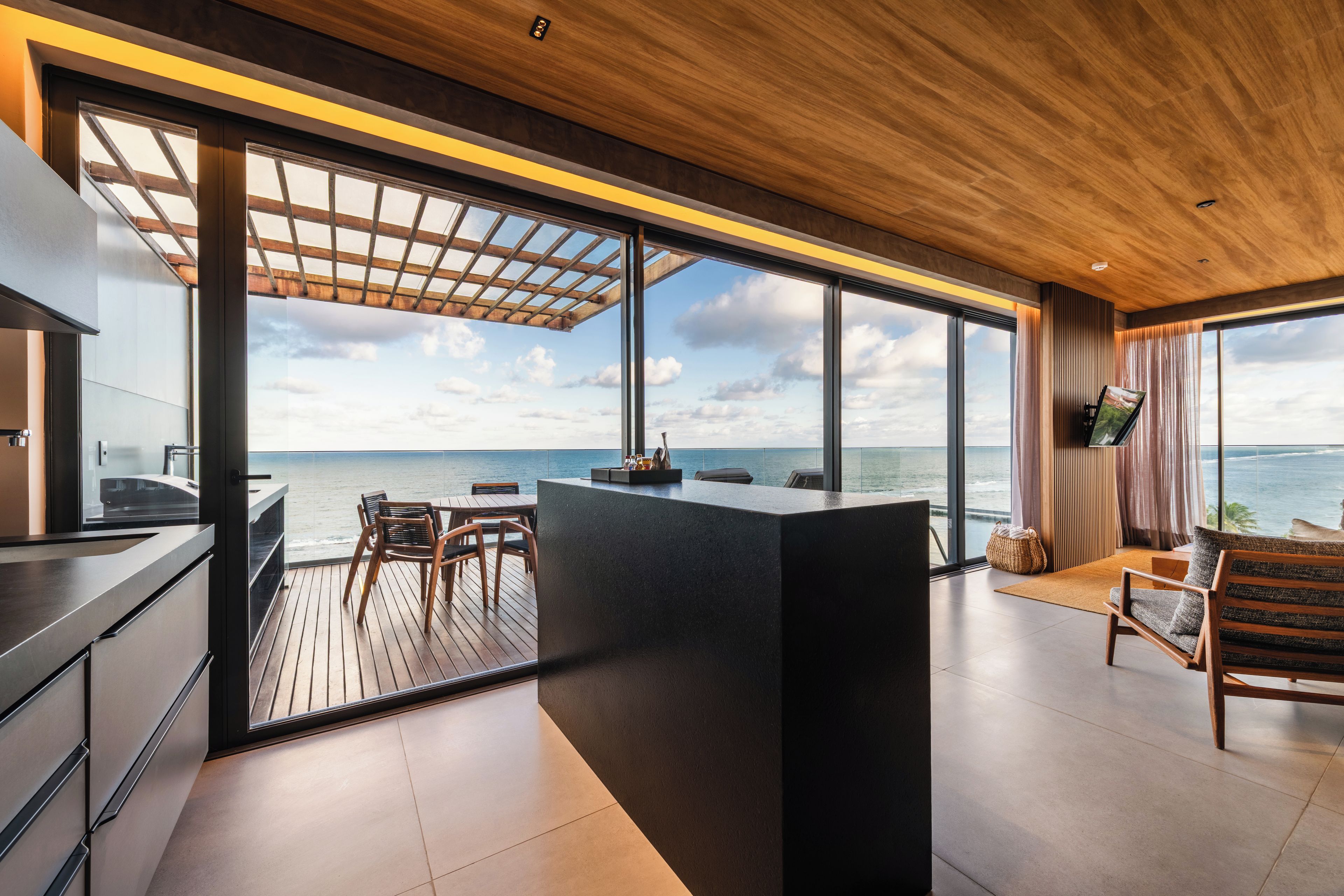A modern kitchen with a view of the ocean, a wooden deck, and a large window.