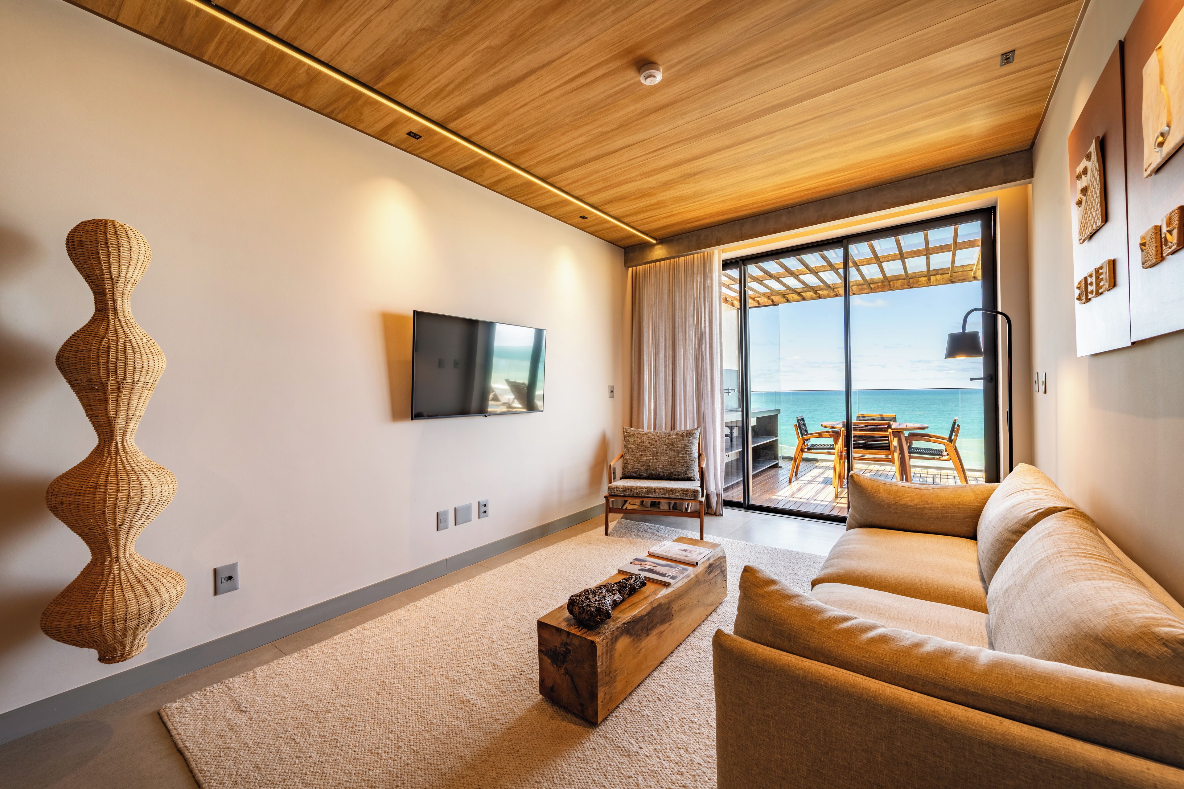 Una sala moderna con un televisor de pantalla plana, una escultura de mimbre, un sofá y vistas al mar a través de grandes puertas de cristal.