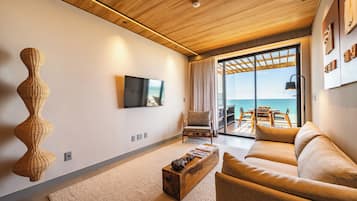 Una sala moderna con un televisor de pantalla plana, una escultura de mimbre, un sofá y vistas al mar a través de grandes puertas de cristal.