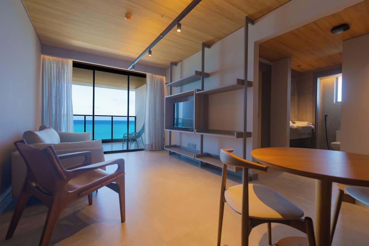 Une chambre d’hôtel moderne dotée d’une grande fenêtre, d’un coin salon avec une table et des chaises, et d’étagères intégrées.