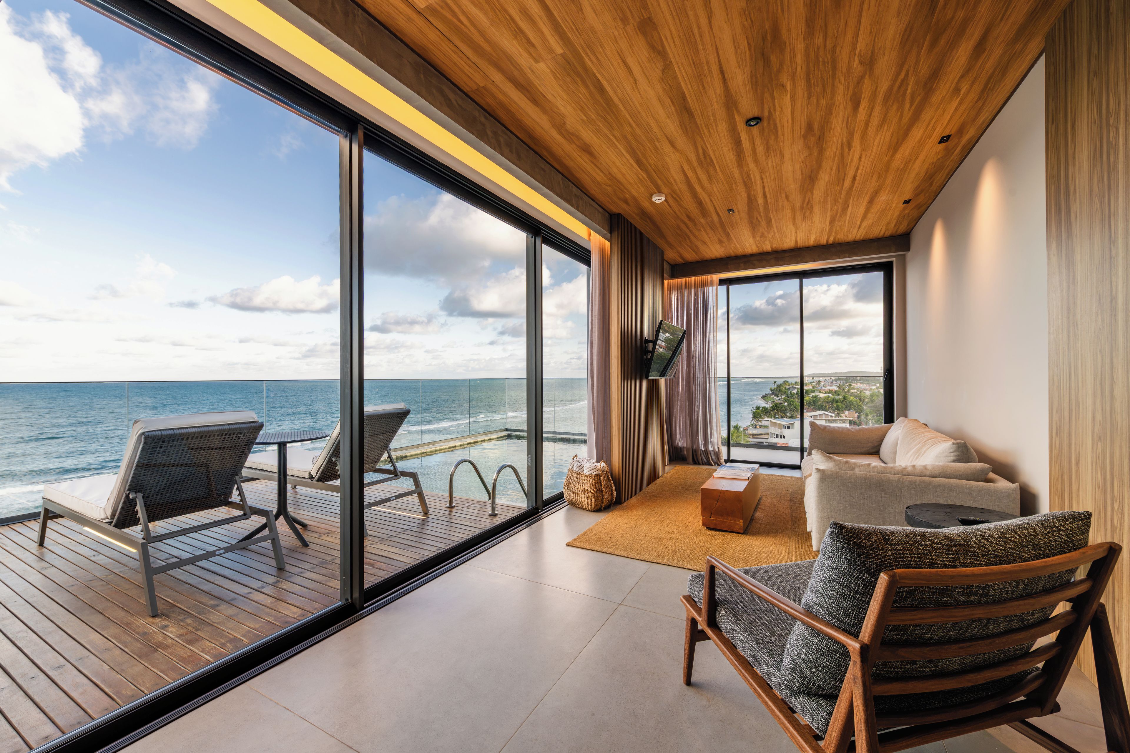 A modern interior with a large window overlooking the sea, a wooden ceiling, and a furnished living area.