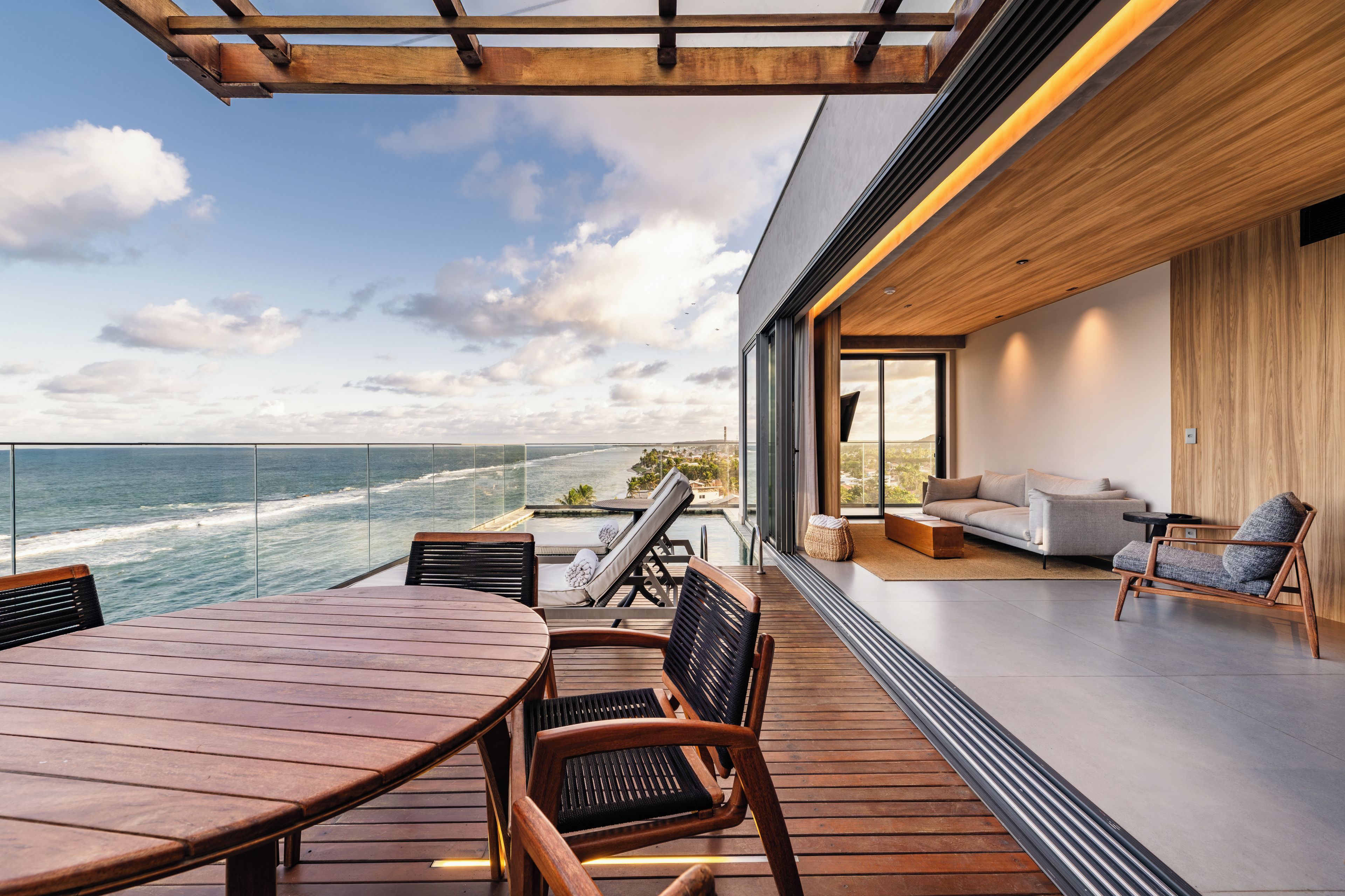 Una terraza moderna al aire libre con mesa y sillas de madera, con vistas a una playa y el océano.
