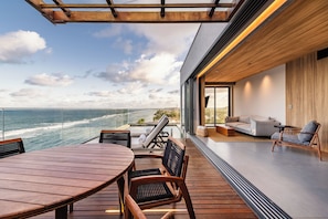 A modern outdoor deck with a wooden table and chairs, overlooking a beach and ocean. - Ritz Barra de São Miguel (Barra de São Miguel)