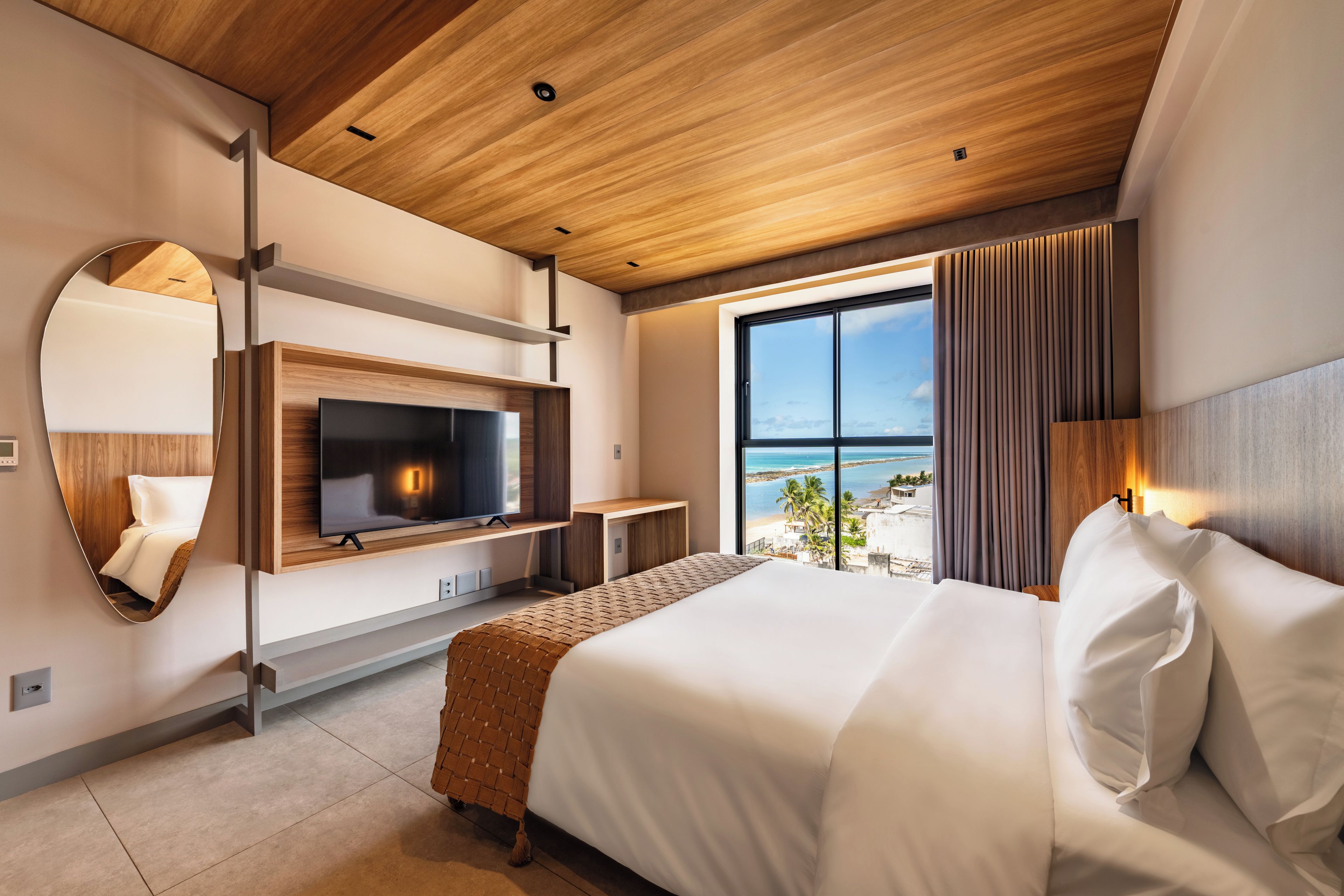 Una habitación de hotel moderna con una cama grande, televisión y vistas a la playa, además de un techo de madera.