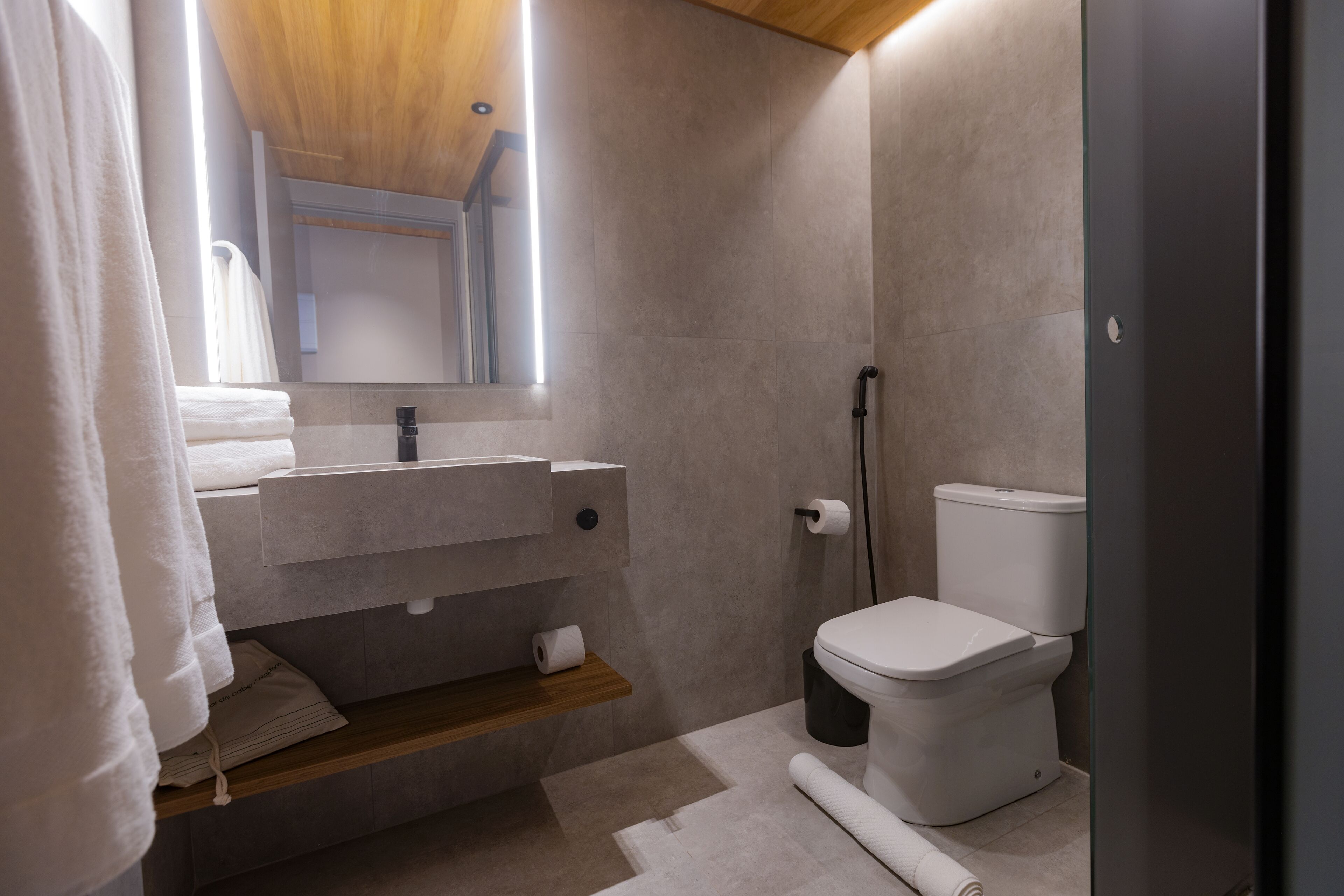 A modern bathroom with a wooden ceiling, a built-in sink, a toilet, and a mirror.