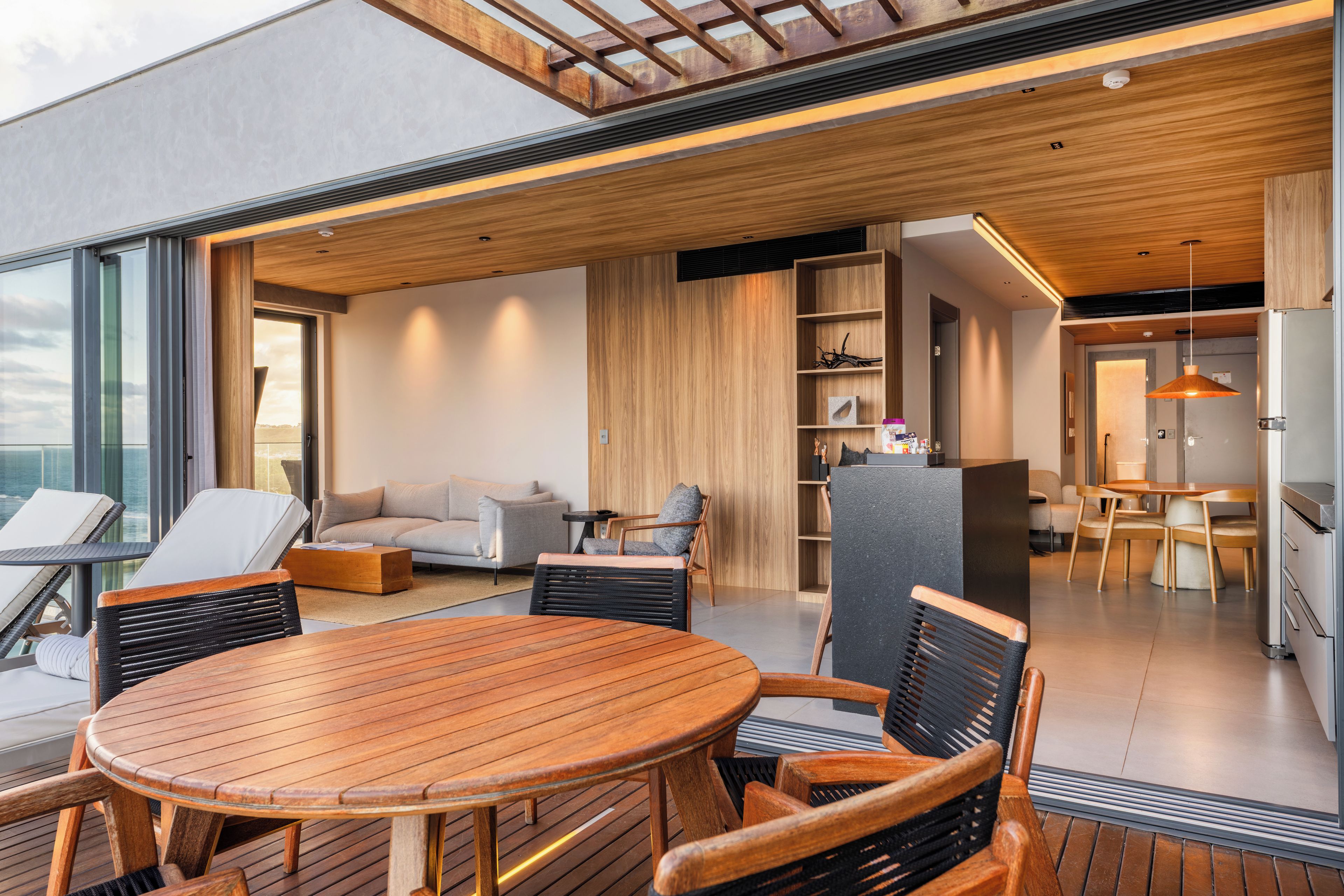 A modern interior with a wooden dining table, chairs, a sofa, and a kitchen area.