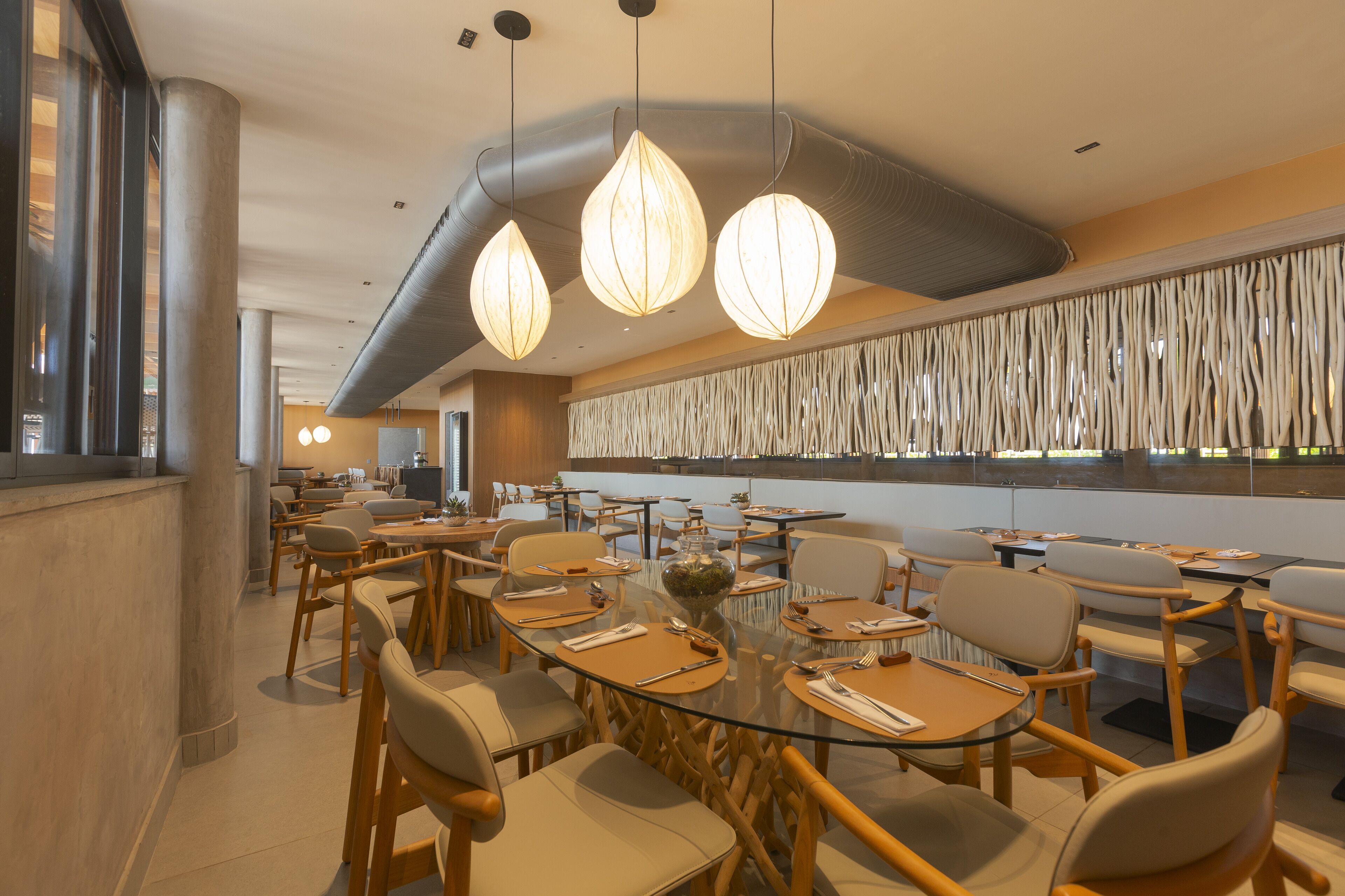Un espace de restauration moderne avec des tables rondes, des chaises en bois et des luminaires suspendus.