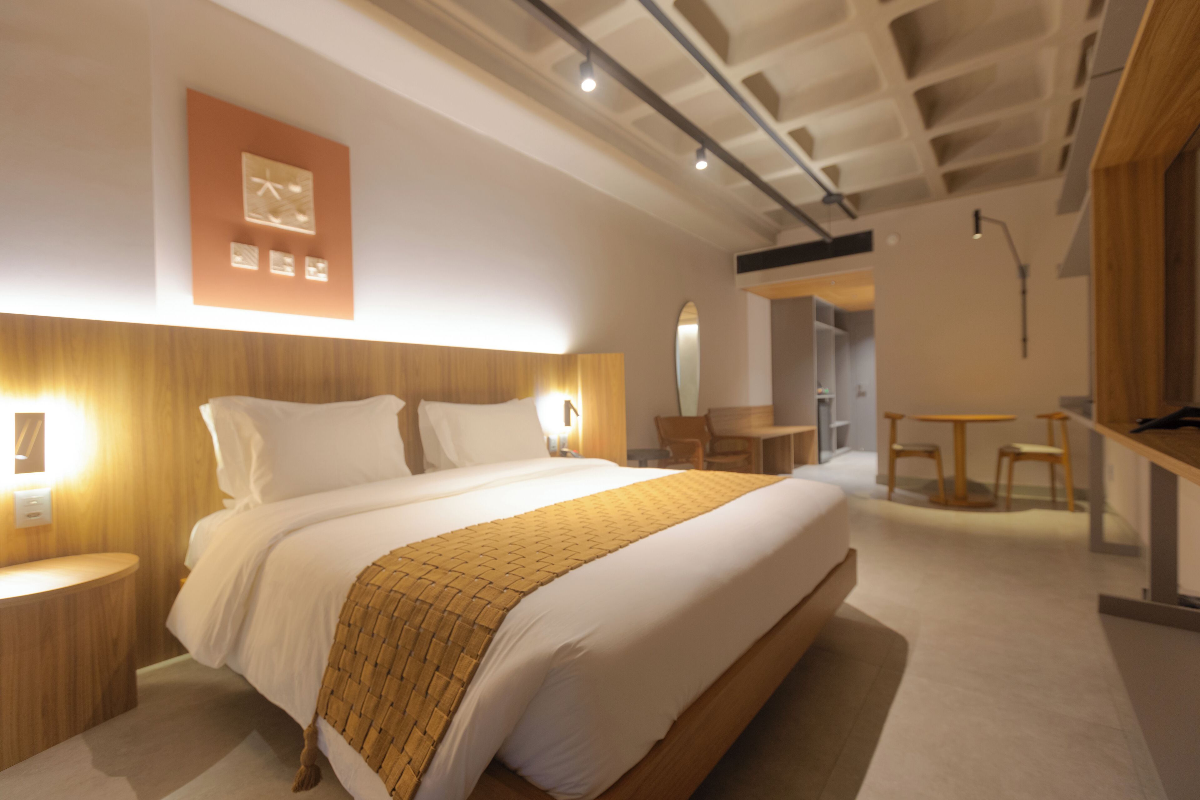 A modern hotel room with a large bed, bedside tables, a desk, and a chair.