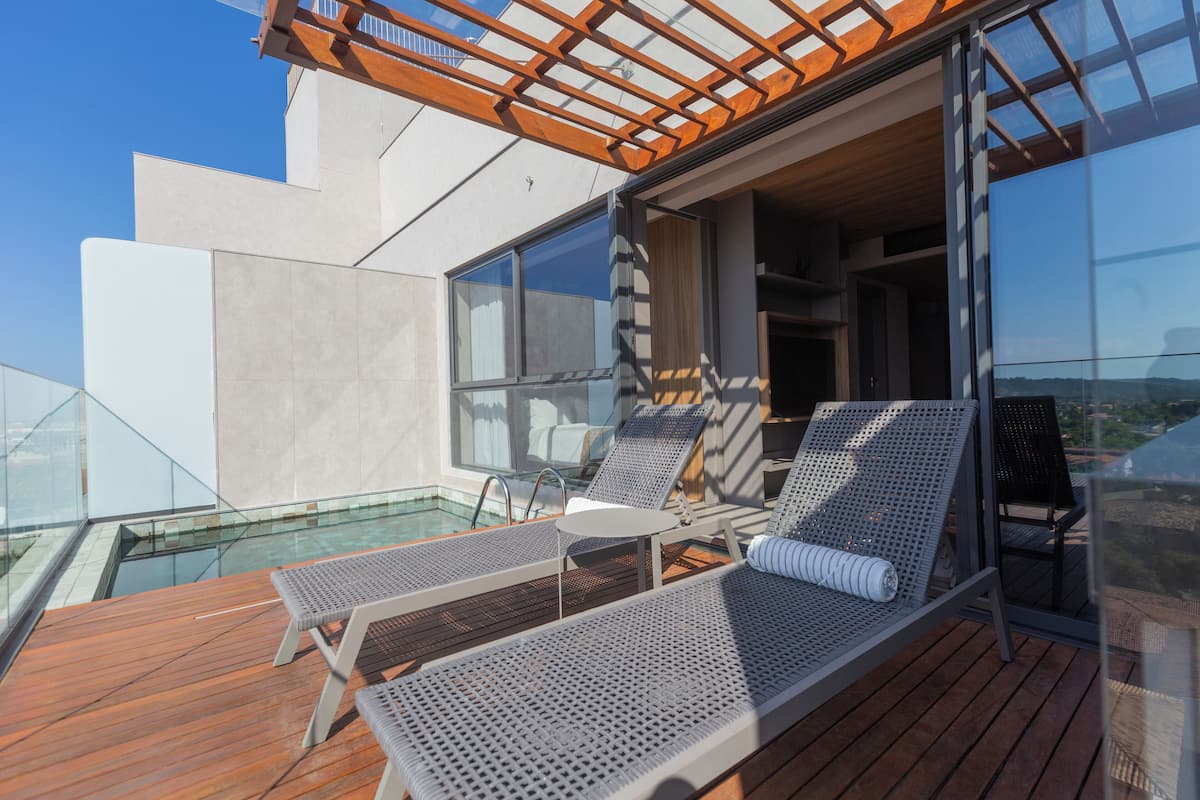 Une terrasse extérieure moderne, dotée de deux chaises longues, d’une petite table et d’une balustrade en verre.