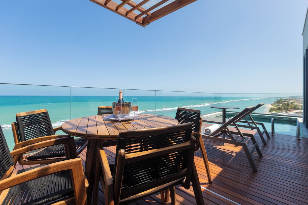 Une terrasse en bois avec une table ronde et des chaises, donnant sur un océan d’un bleu limpide.
