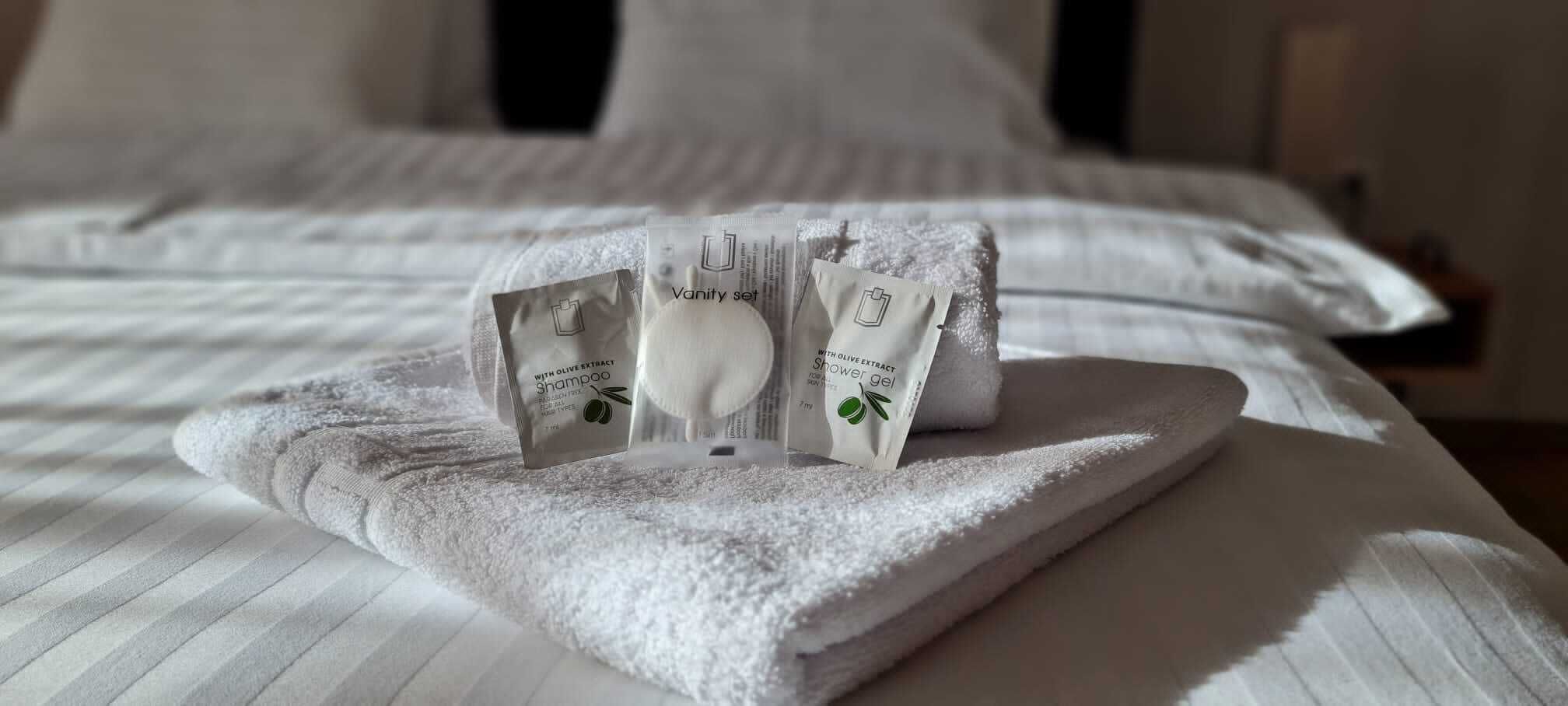 En snyggt bäddad säng med ett vitt handduk och hygienartiklar, inklusive schampo och duschgel.