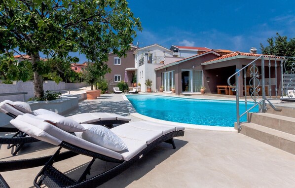 Relax by the pool surrounded by lounge chairs and sun loungers, with a view of the surrounding area from the adjacent building's balcony.