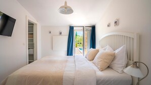 A bedroom with a bed, a TV mounted on the wall, a bedside lamp, and a view of the outdoors through a sliding door.