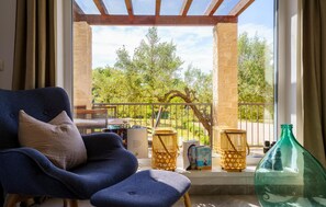 Ein Zimmer mit blauem Sessel, einem kleinen Tisch und Blick auf einen Balkon mit Geländer und Pflanzen.