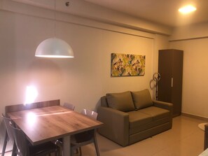 A modern living room with a wooden dining table, a sofa, a painting on the wall, and a ceiling light.