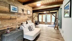 L’intérieur d’un chalet accueillant, avec un mur en bois, un canapé blanc, une commode et des tableaux encadrés.