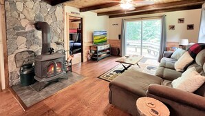 Un salon chaleureux avec une cheminée en pierre, un plafond en bois et une grande fenêtre donnant sur l’extérieur.
