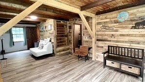 Une pièce rustique aux murs en bois et au plafond en pente, avec un lit, un banc et une enseigne sur laquelle on peut lire « Maine Maine ».