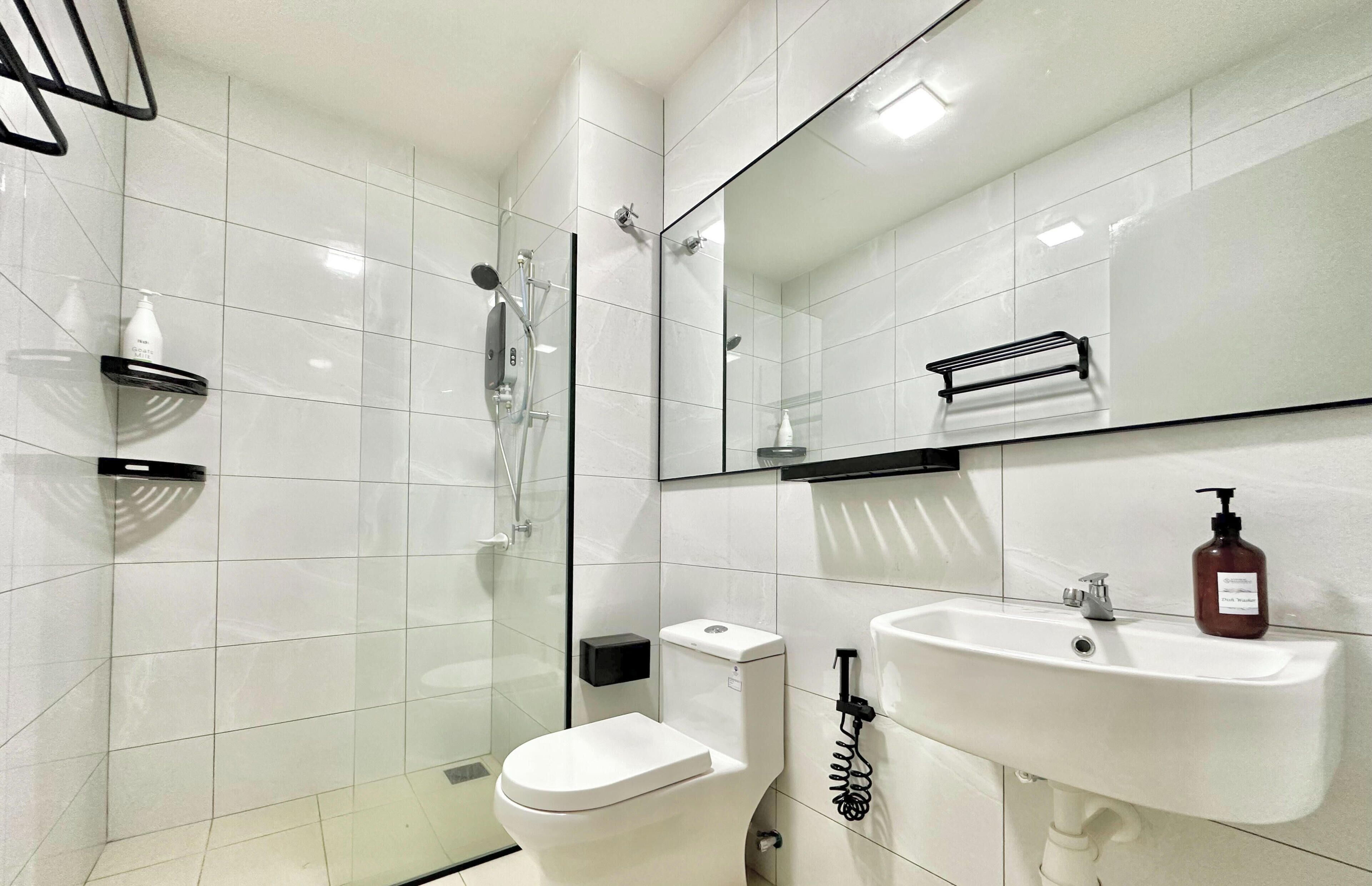 A modern bathroom with a glass-enclosed shower, a white toilet, and a sink with a soap dispenser.