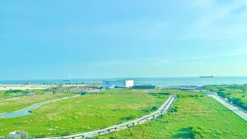 An aerial view of a coastal area with a large white building, green fields, and a road leading to the sea.