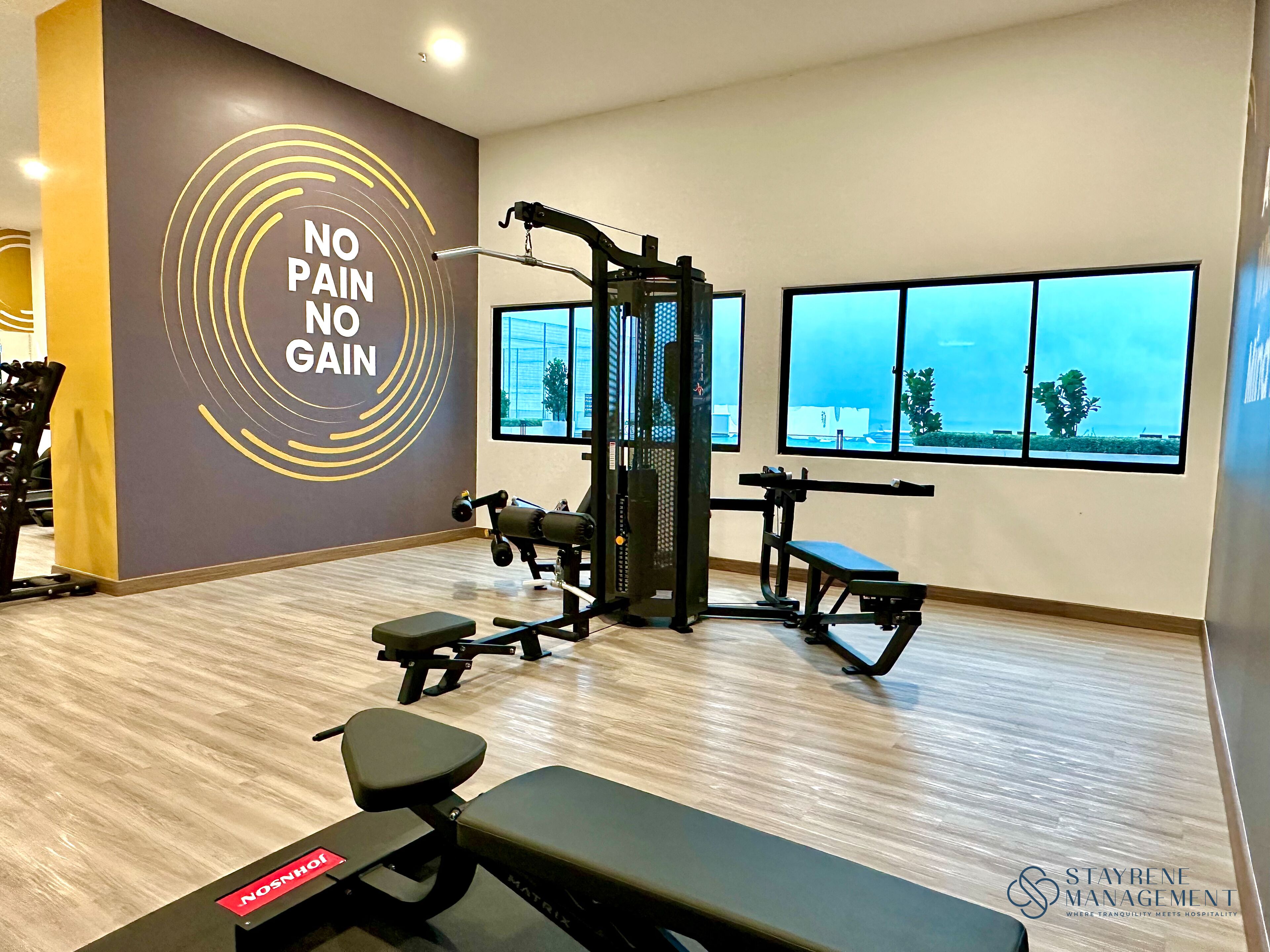 A gym with exercise equipment, a wall with motivational text, and large windows with a view.