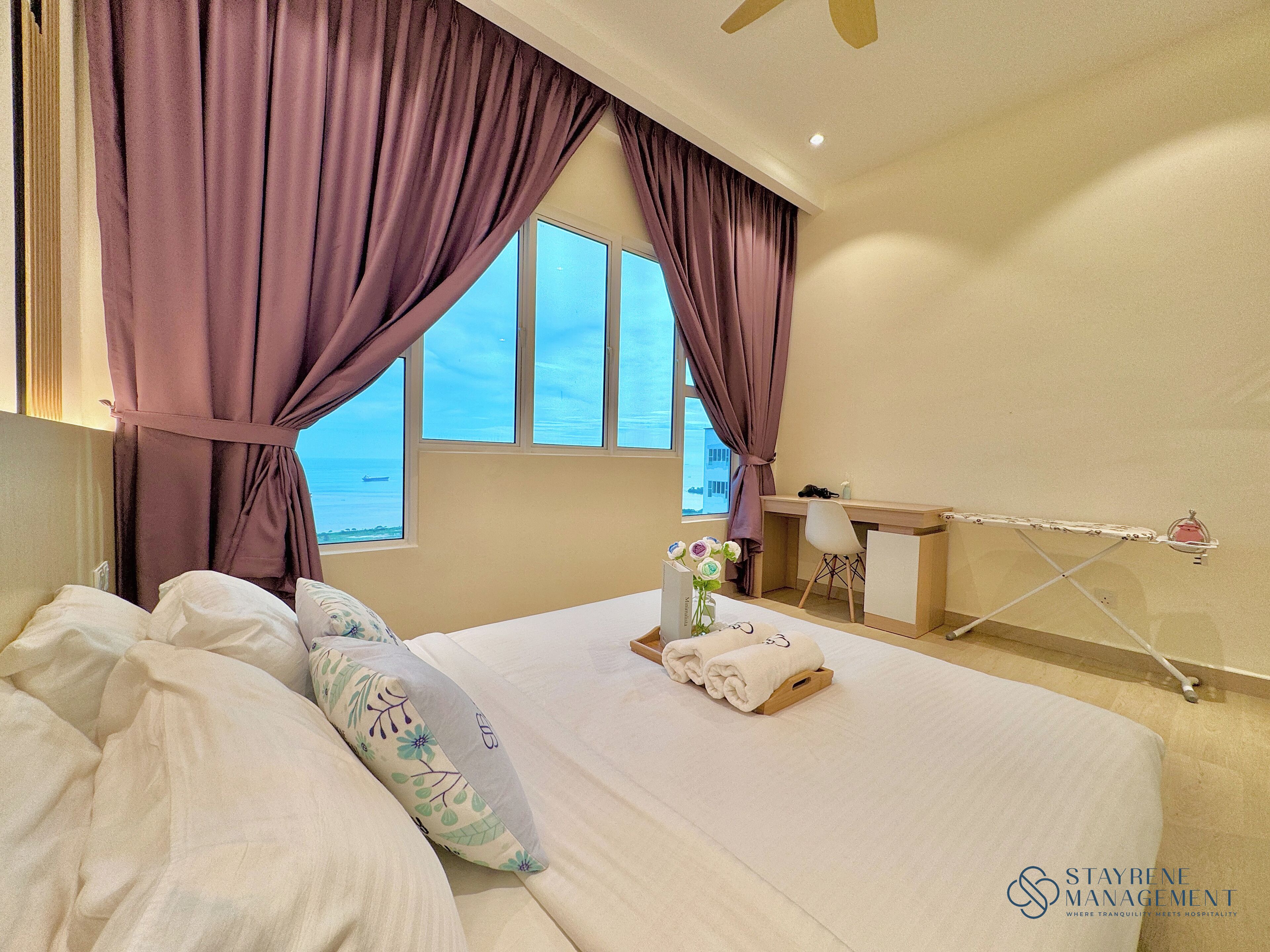 A hotel room with a bed, a desk, and a view of the sea.