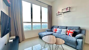 A modern living room with a grey sofa, two small round tables, and a flat-screen TV on a stand.