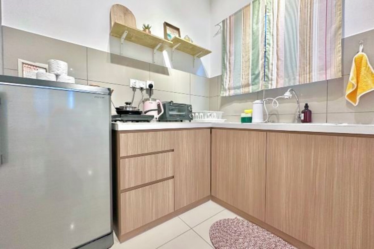 Una cocina con refrigerador, tostadora, hervidor y pileta. Hay alacenas de madera y una encimera.