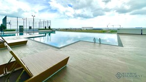 A rooftop pool area with lounge chairs, a basketball hoop, and a view of the city skyline. - Amber Cove Melaka Sea View by Stayrene (Malacca City)