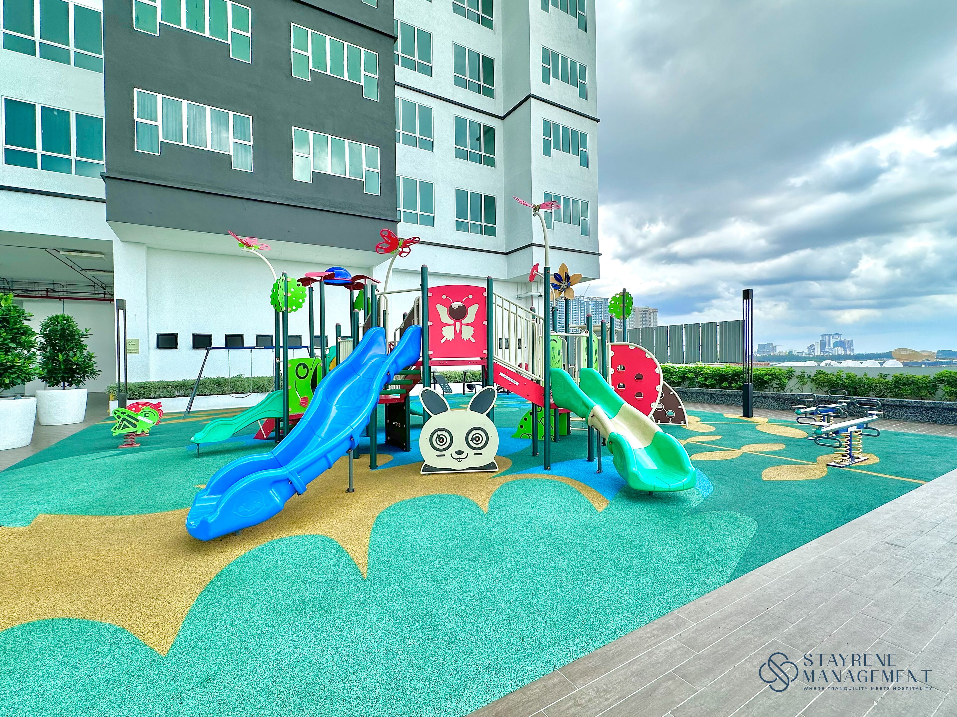 Un'area giochi per bambini con scivoli e strutture per arrampicarsi, circondata da un edificio con numerose finestre.
