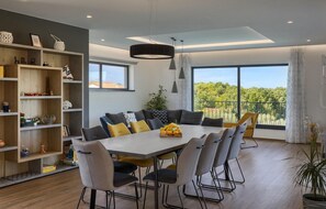 Een moderne eethoek met een grote tafel, stoelen en uitzicht op groen door grote ramen.