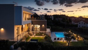 Ein modernes, zweistöckiges Haus mit Balkon, Schwimmbad und einer gut beleuchteten Gartenanlage.