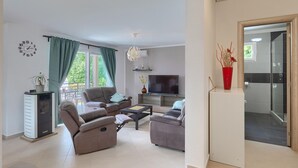 Ein modernes Wohnzimmer mit einer Couch, Sesseln, einem Fernseher und einem Kamin.