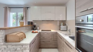 Eine moderne Küche mit weißen Schränken, einer Wand mit Steinverkleidung, einem eingebauten Backofen und einem Fenster mit Vorhängen.