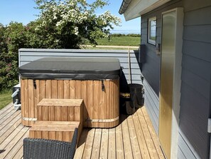 Un bain à remous avec une structure extérieure en bois, une terrasse en bois et une maison avec une fenêtre.