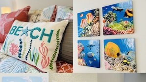 Dekoration im Strandhausstil mit Kissen, Wandkunst, einem Gemälde eines Bootes am Strand, einer Muschel und einem Seestern.