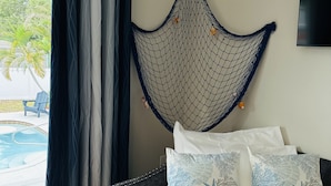 Ein Schlafzimmer mit Bett, Kissen, einer Hängematte und Blick auf einen Swimmingpool.