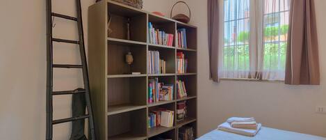 A bedroom with a bed, a bookshelf, a ladder, and a window with curtains.