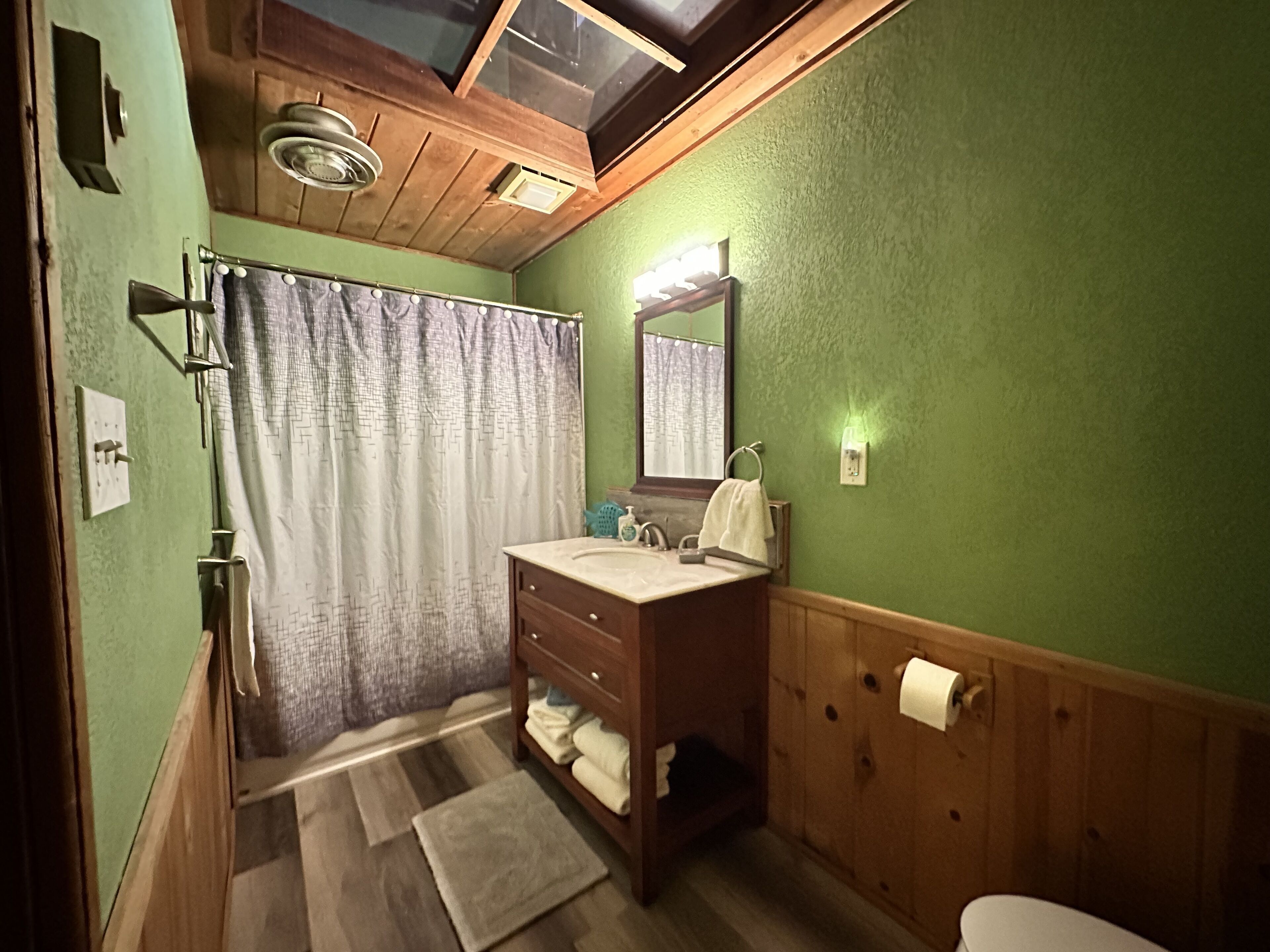 Un baño con tocador de madera, cortina de ducha, espejo y retrete.
