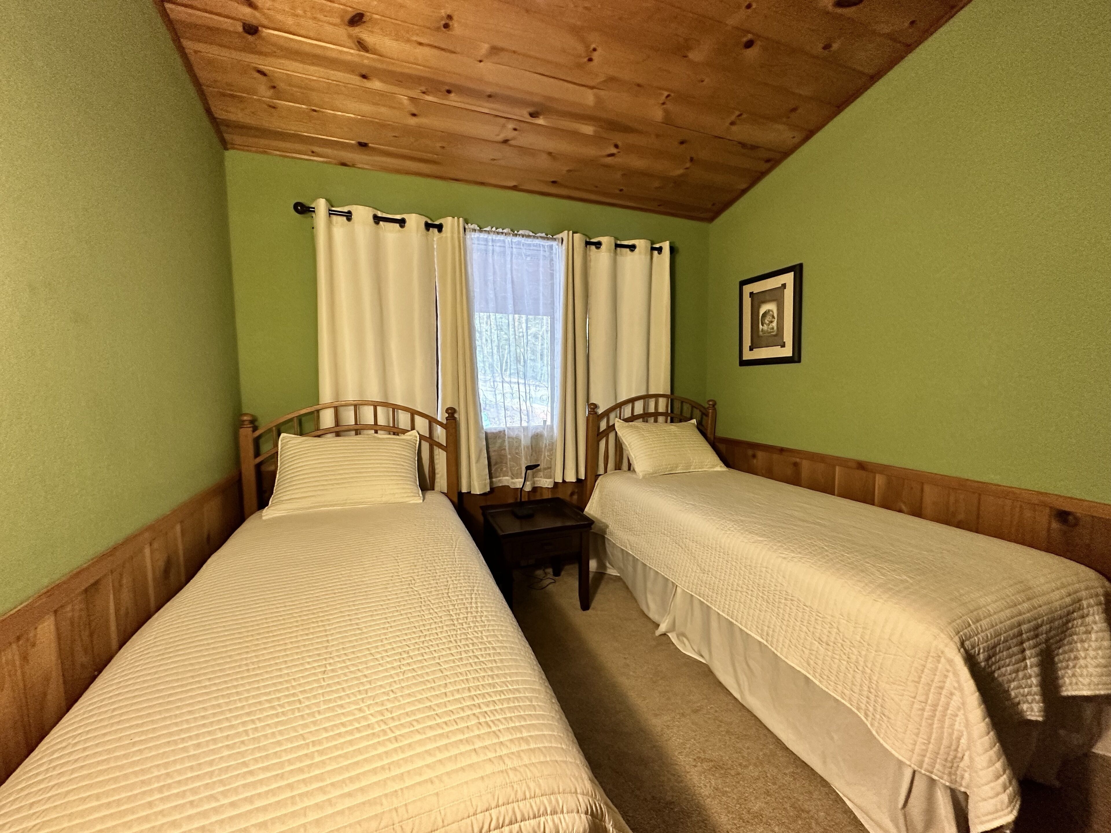 Ein Zimmer mit zwei Holzbetten, einer Holzbalkendecke und einem Fenster mit Vorhängen.