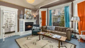 A living room with a fireplace, a sofa, a coffee table, and a view of a balcony. - Artistic Victorian Gem in a Trendy neighborhood (Portland)