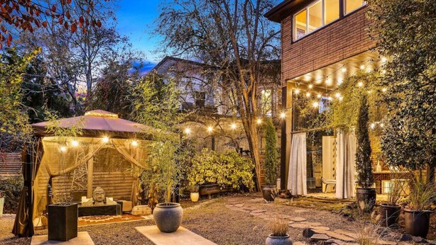 A well-lit outdoor patio area with a wooden pergola, potted plants, and string lights. - Artistic Victorian Gem in a Trendy neighborhood (Portland)