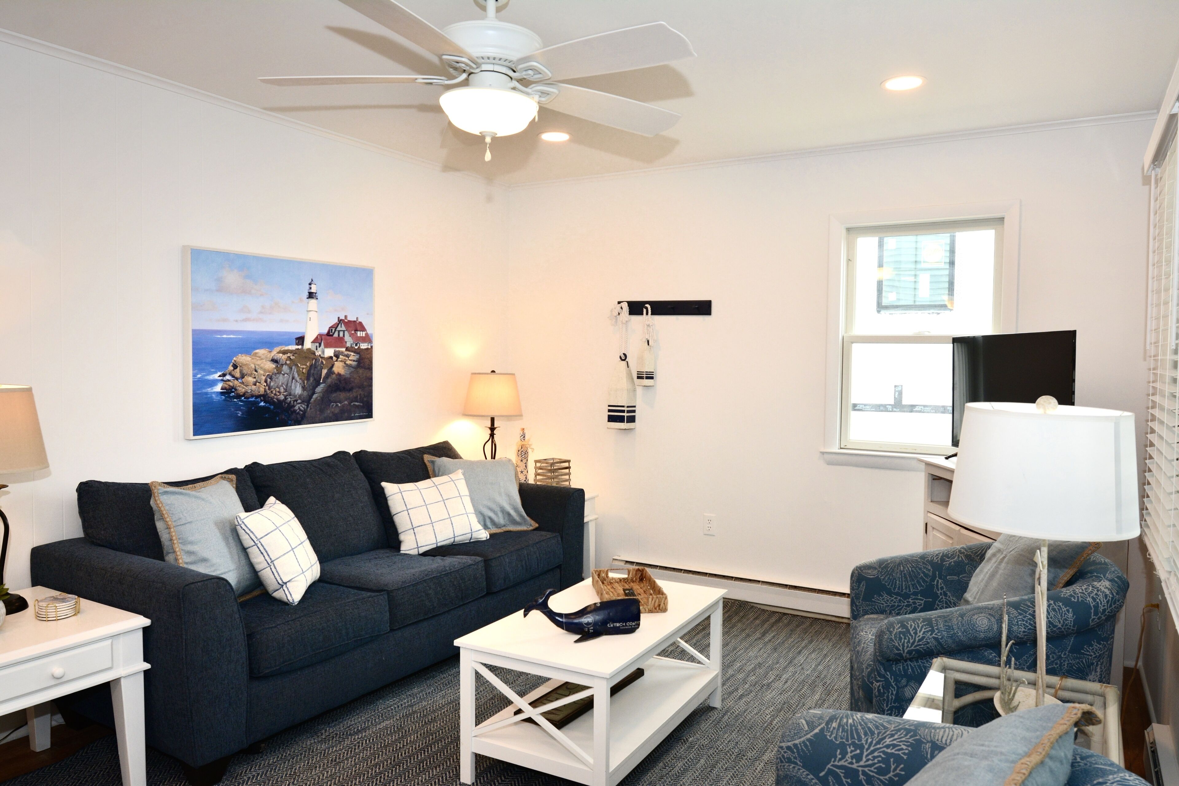 A modern living room with a dark blue sofa, a white coffee table, a blue armchair, and a ceiling fan.
