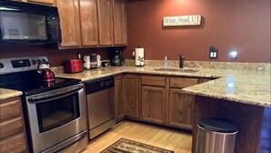 A kitchen with wooden cabinets, a granite countertop, a stainless steel stove, and a trash can.