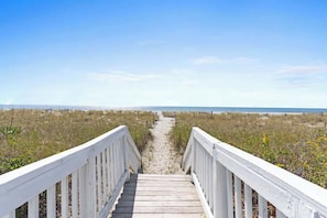 A wooden boardwalk leading to a beach with a clear sky.
