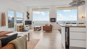 Una sala de estar moderna con un ventanal grande, una zona de cocina y un área de descanso con vista al mar.