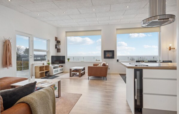 A modern living room with a large window, a kitchen area, and a seating area with a view of the sea.