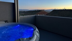 Una vasca idromassaggio su un balcone con vista su un paesaggio collinare e edifici in lontananza.